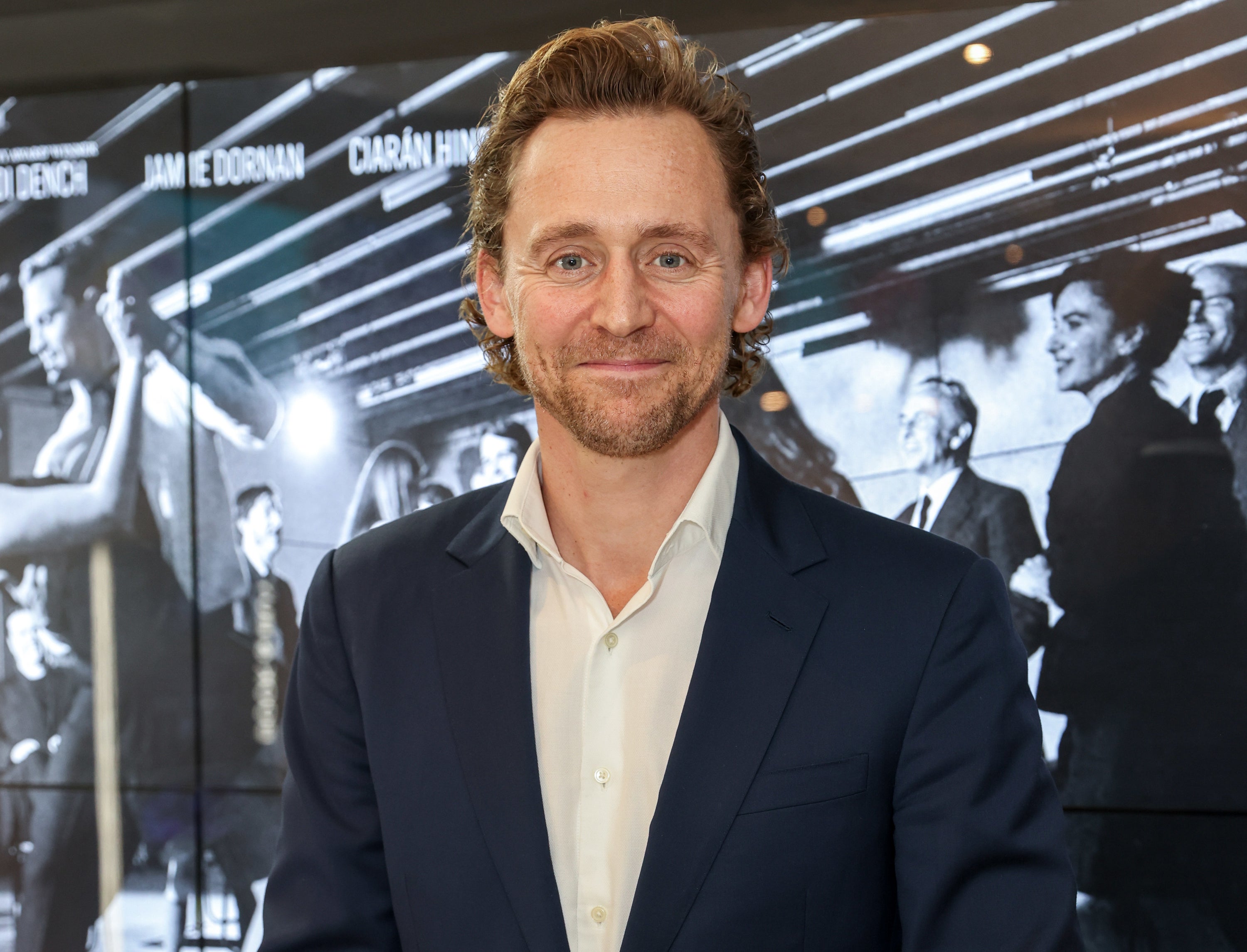 A close-up of Tom smiling and wearing a jacket and shirt, no tie