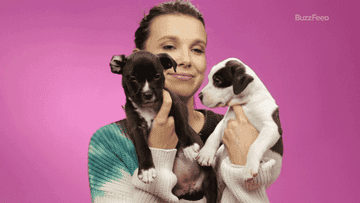 Millie Bobby Brown holding puppies close to her face and smiling