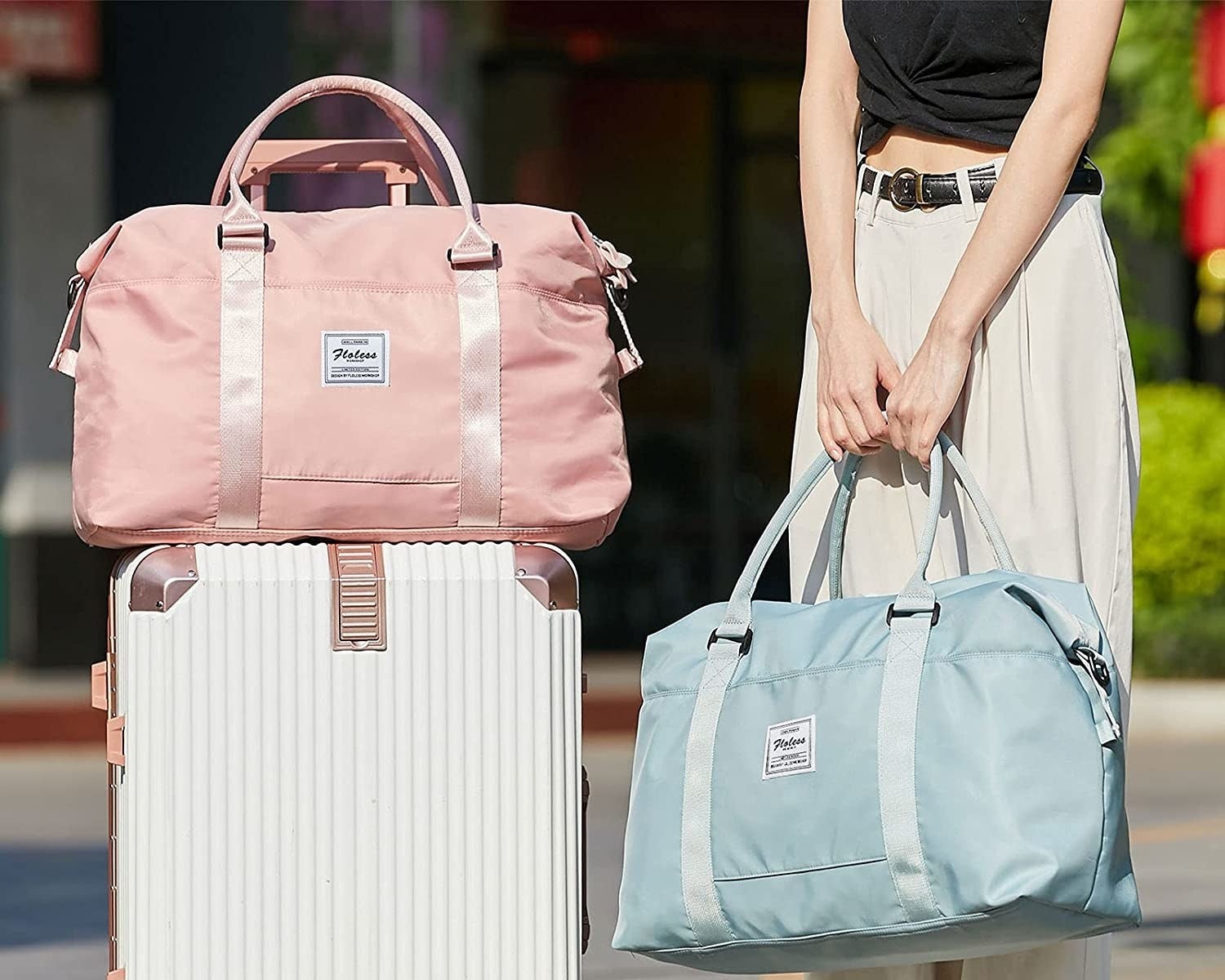 A person standing carrying one of the bags with another stacked on top of a suitcase beside them