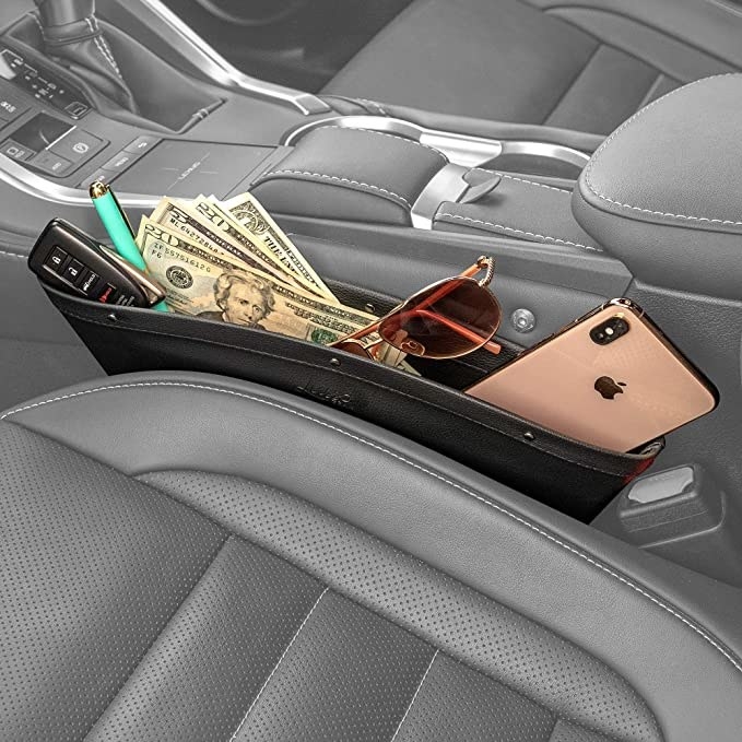 The organizer with money, keys, sunglasses, and a phone in it in the gap between the front seat and a console