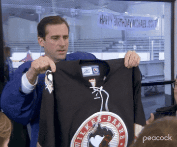 Michael Scott holding up a jersey that reads &quot;From Dwight&quot; on the back.