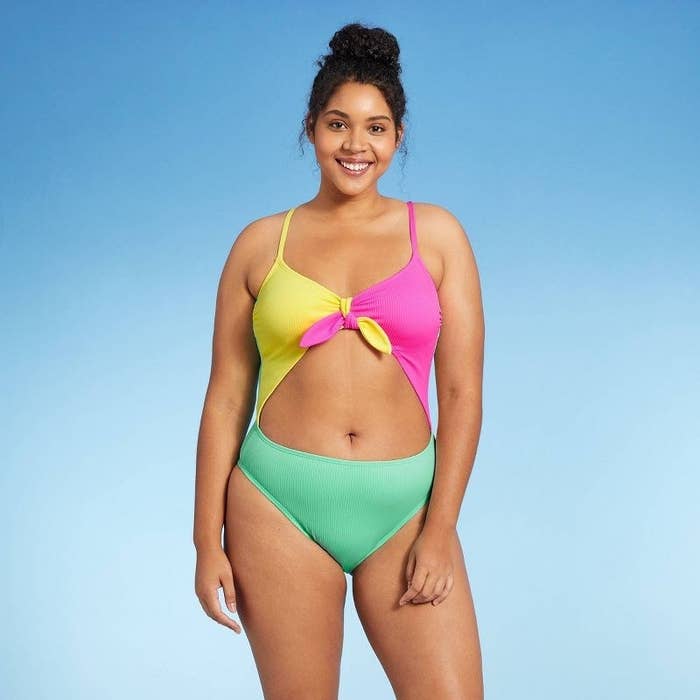 a model wearing cutout one-piece swimsuit with yellow and pink orange tie top, green bottom