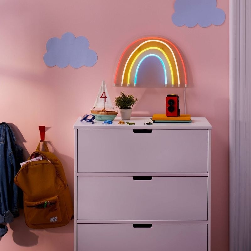 Neon raibow light on pink wall over dresser