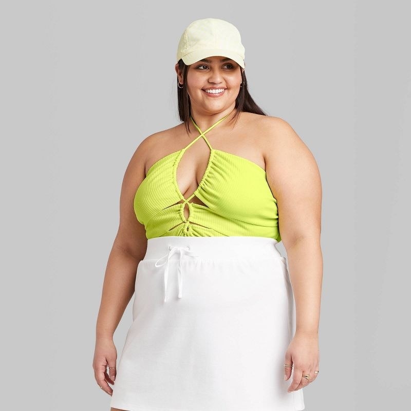 Model wearing lime green halter with white skirt and white hat