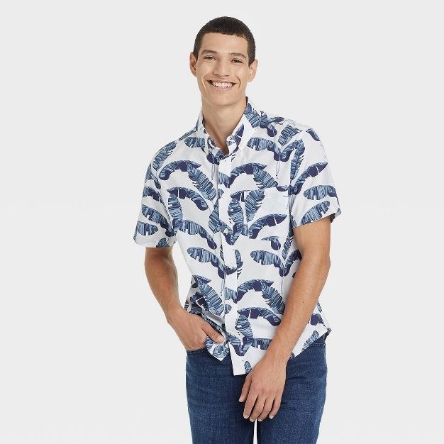 The model wears the white button-up that has blue palm fronds