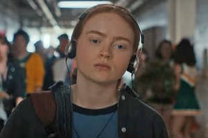 Max from Stranger Things walking down the school hallway with headphones over her ears