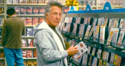 Dustin Hoffman in a video store looking annoyed