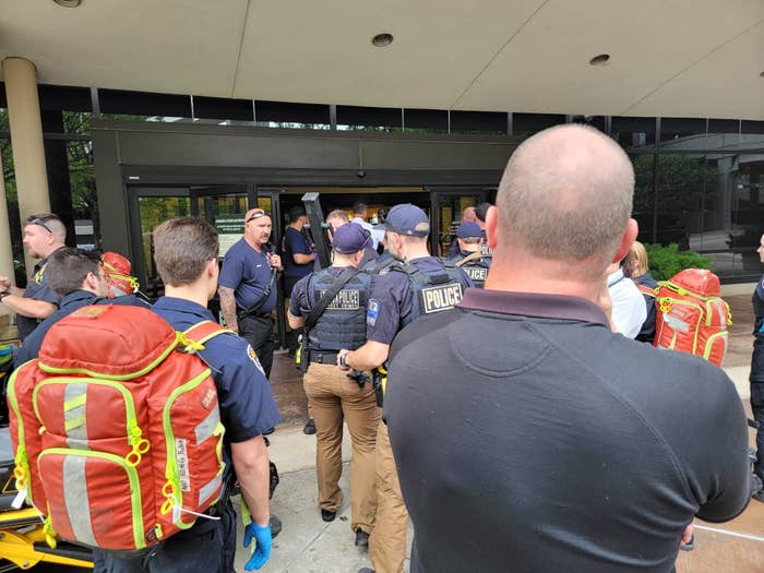 Police officers and first responders wearing large neon backpacks walk toward a hospital entrance