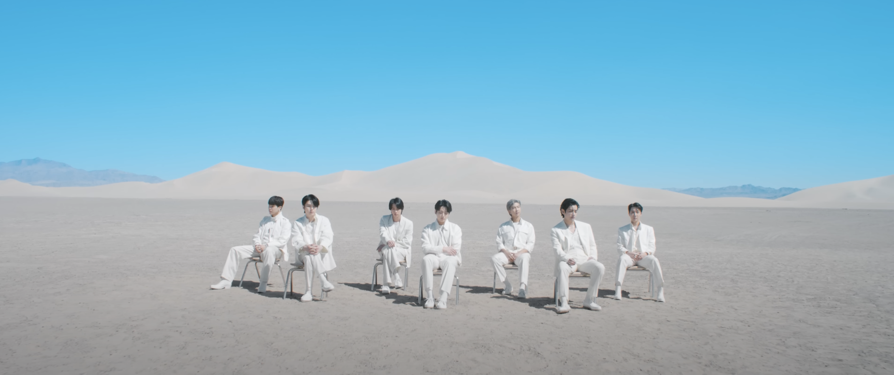 Members of BTS sit in a white sandy desert