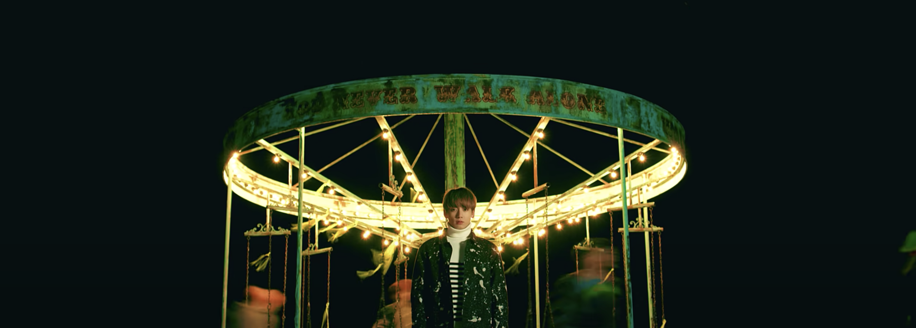 A still from a music video shows a carousel with the words &quot;you never walk alone&quot; on it
