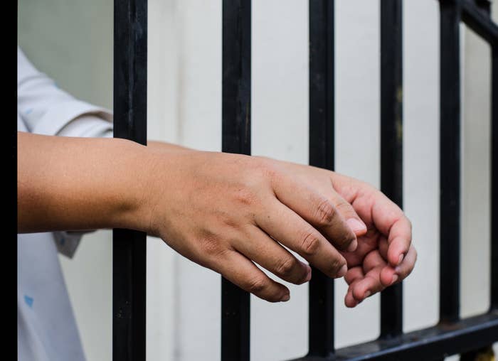 a person&#x27;s hands going through jail bars