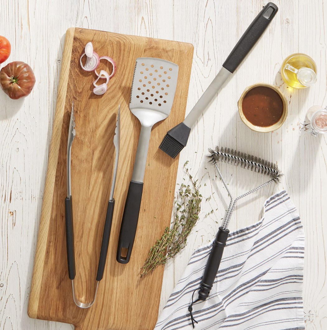 silver and black grilling tools on table with wooden cutting board and condiments