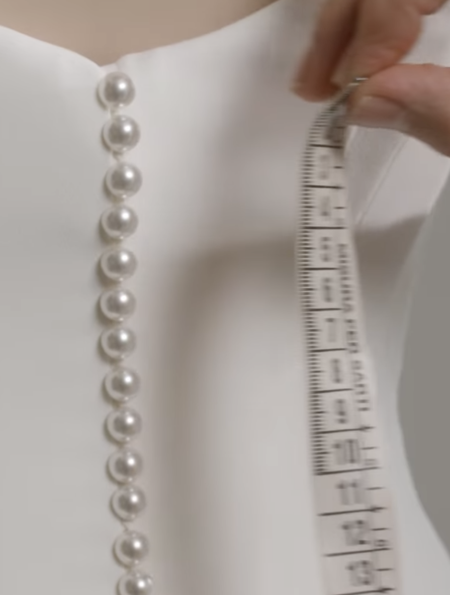 A line of pearls on a dress next to a measuring tape