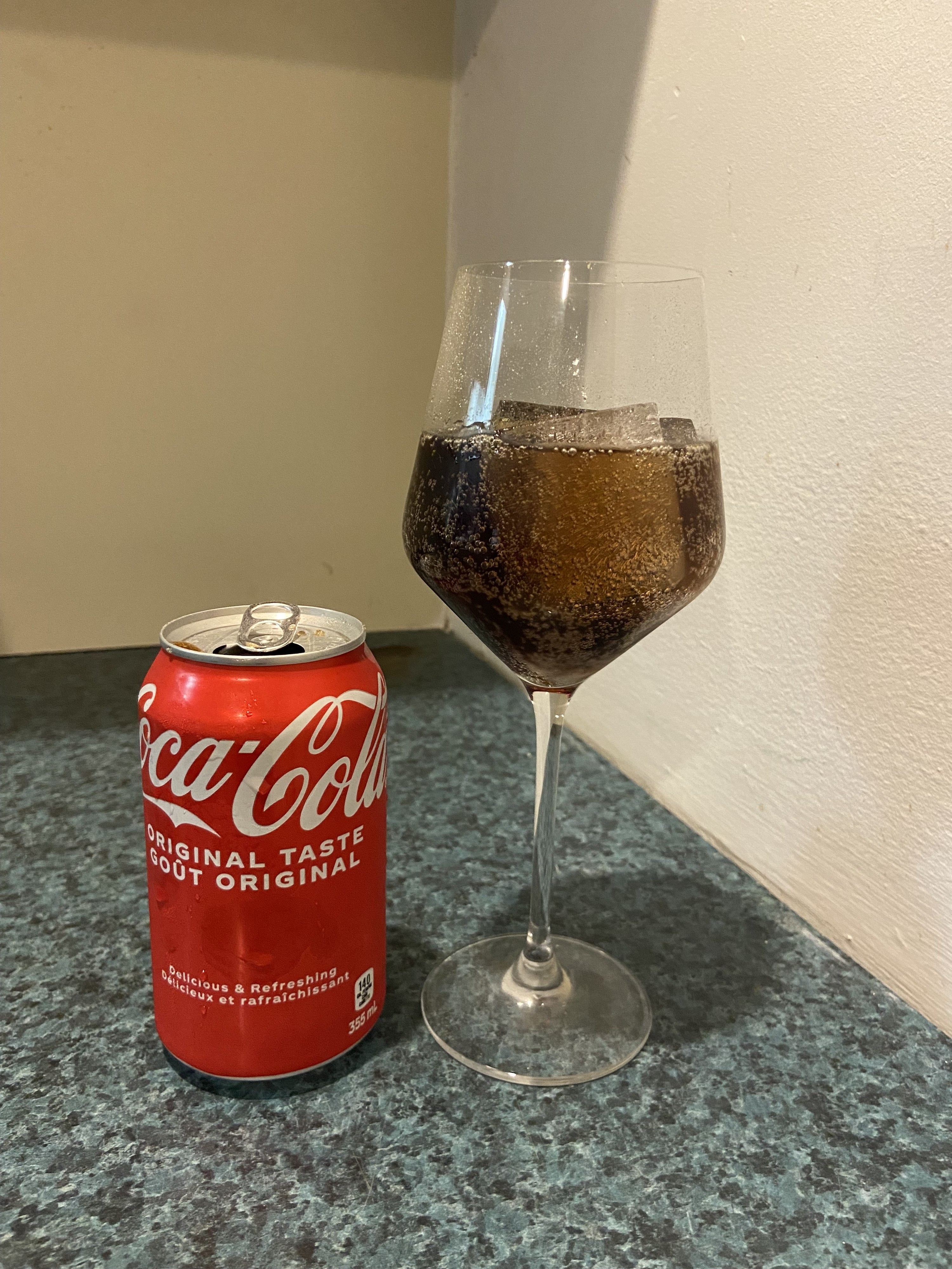 A glass of Coke with a can of Coca-Cola next to it