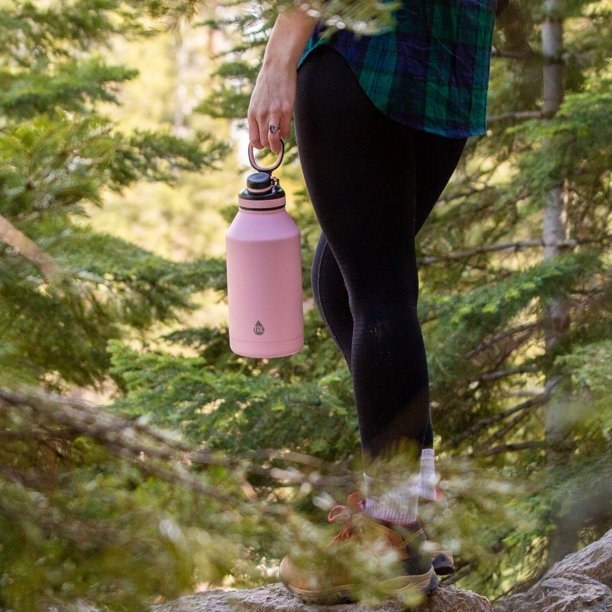 a model holding the pink water bottle on a hike