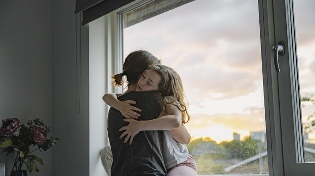 A mom hugs her daughter by a window