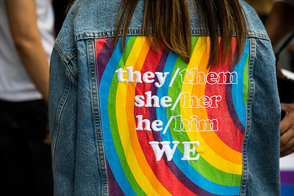 The back of someone&#x27;s jacket reads &quot;they/them, she/her, he/him, we&quot;