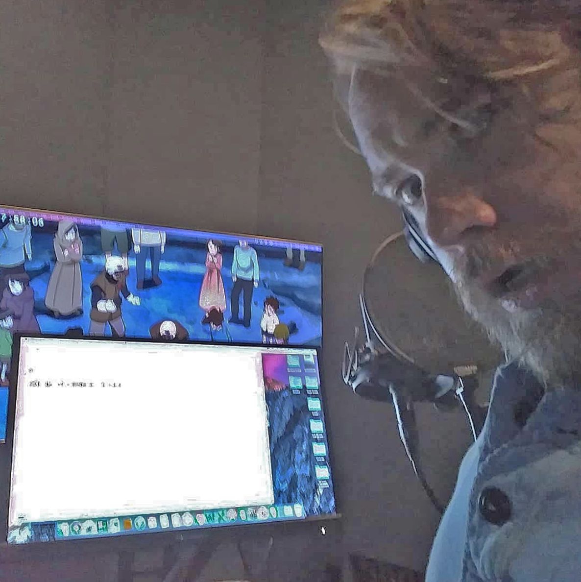 Austin Tindle in a voiceover booth recording dialogue for anime; there are two screens in front of him, one with dialogue and another with anime playing