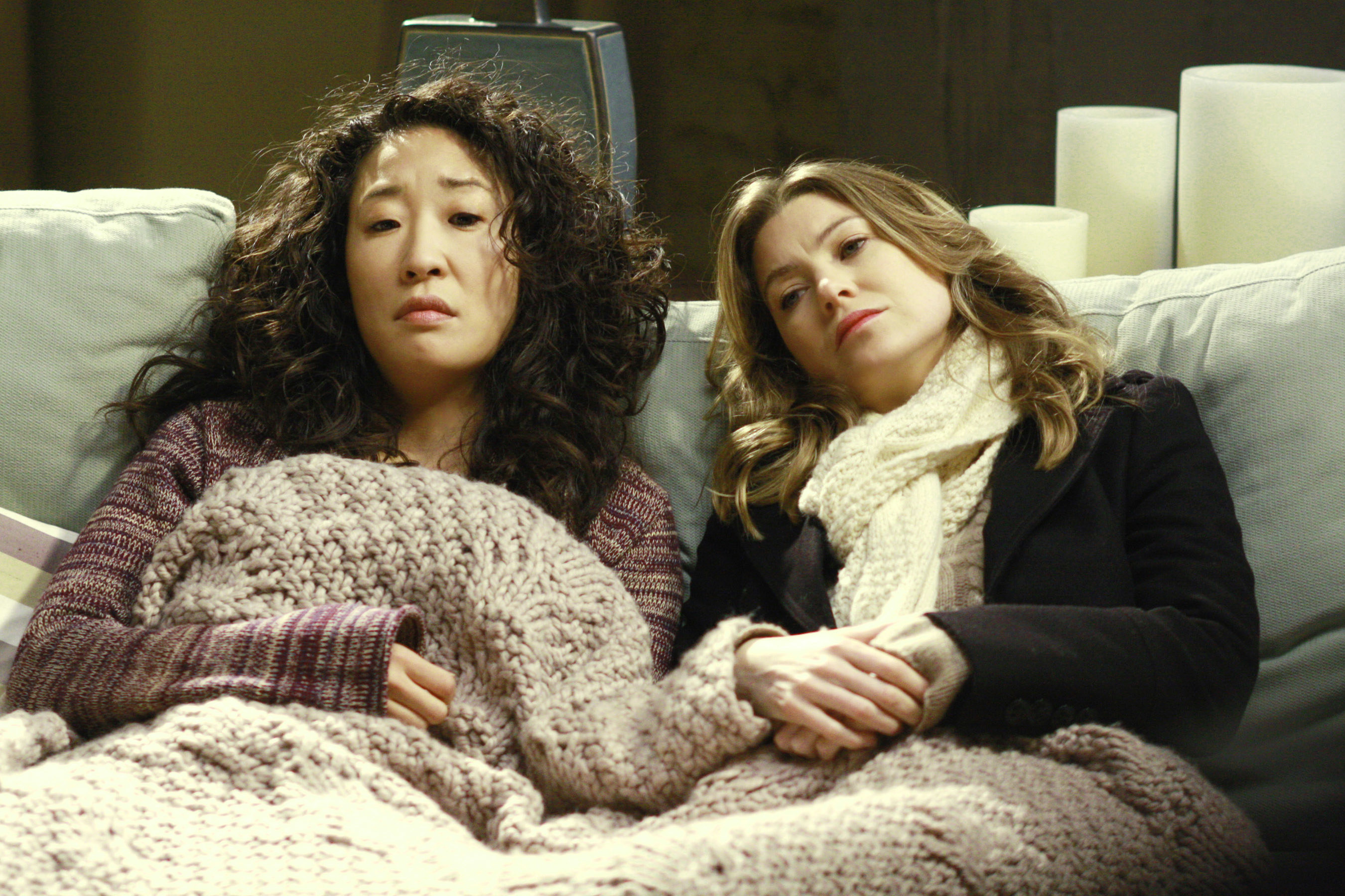sandra oh in Greys anatomy sitting on the couch with a blanket with ellen pompeo