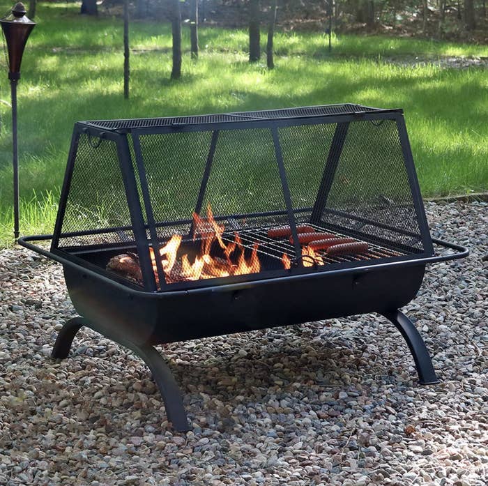 The fire pit in a backyard with hot dogs on the grill