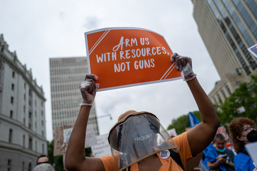 Person holds up a sign reading &quot;Arm us with resources, not guns&quot;