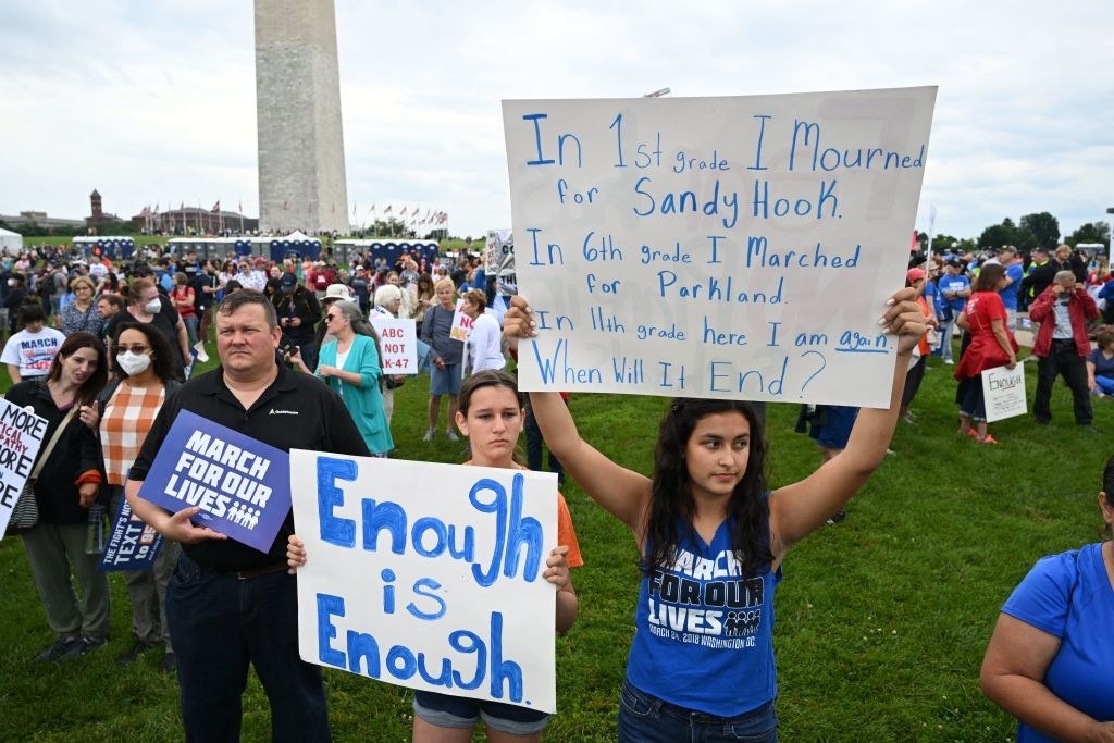 People holding up signs, including &quot;Enough is enough&quot; and &quot;In 6th grade I marched for Parkland; in 11th grade here I am again; when will it end?&quot;