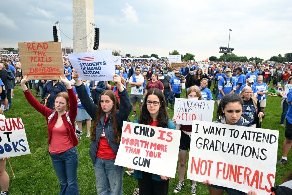 Young people hold up signs, including &quot;A child is worth more than your gun&quot; and &quot;I want to attend graduations not funerals&quot;