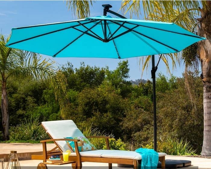 an acacia wood lounge chair in cream under a blue umbrella