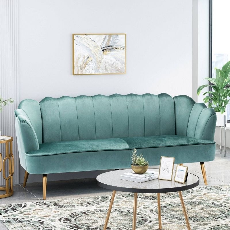 A turquoise and gold three-seater velvet channel shell sofa in a living room