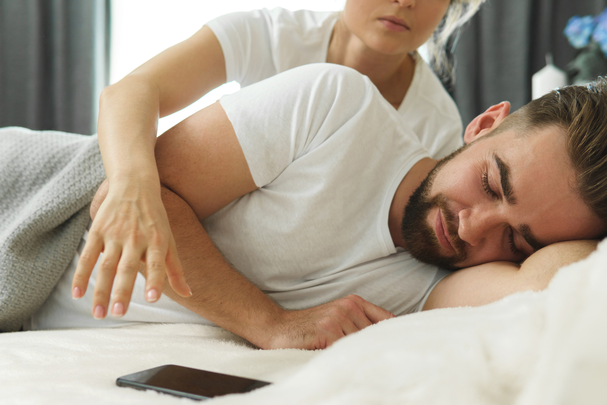 A woman reaches for her sleeping husband&#x27;s phone