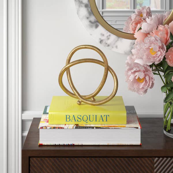 Decorative golden sculpture on books with a pink flower arrangement beside a round mirror on a wooden console table