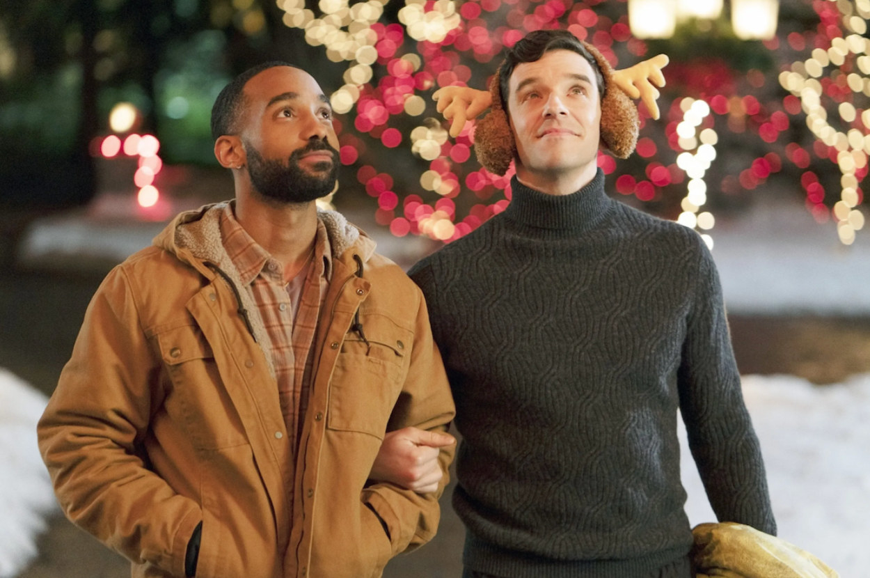 Two men stand arm in arm in a snowy neighbourhood and look at a house off screen