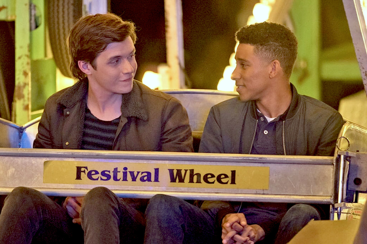 two young men ride a ferris wheel together and gaze at one another