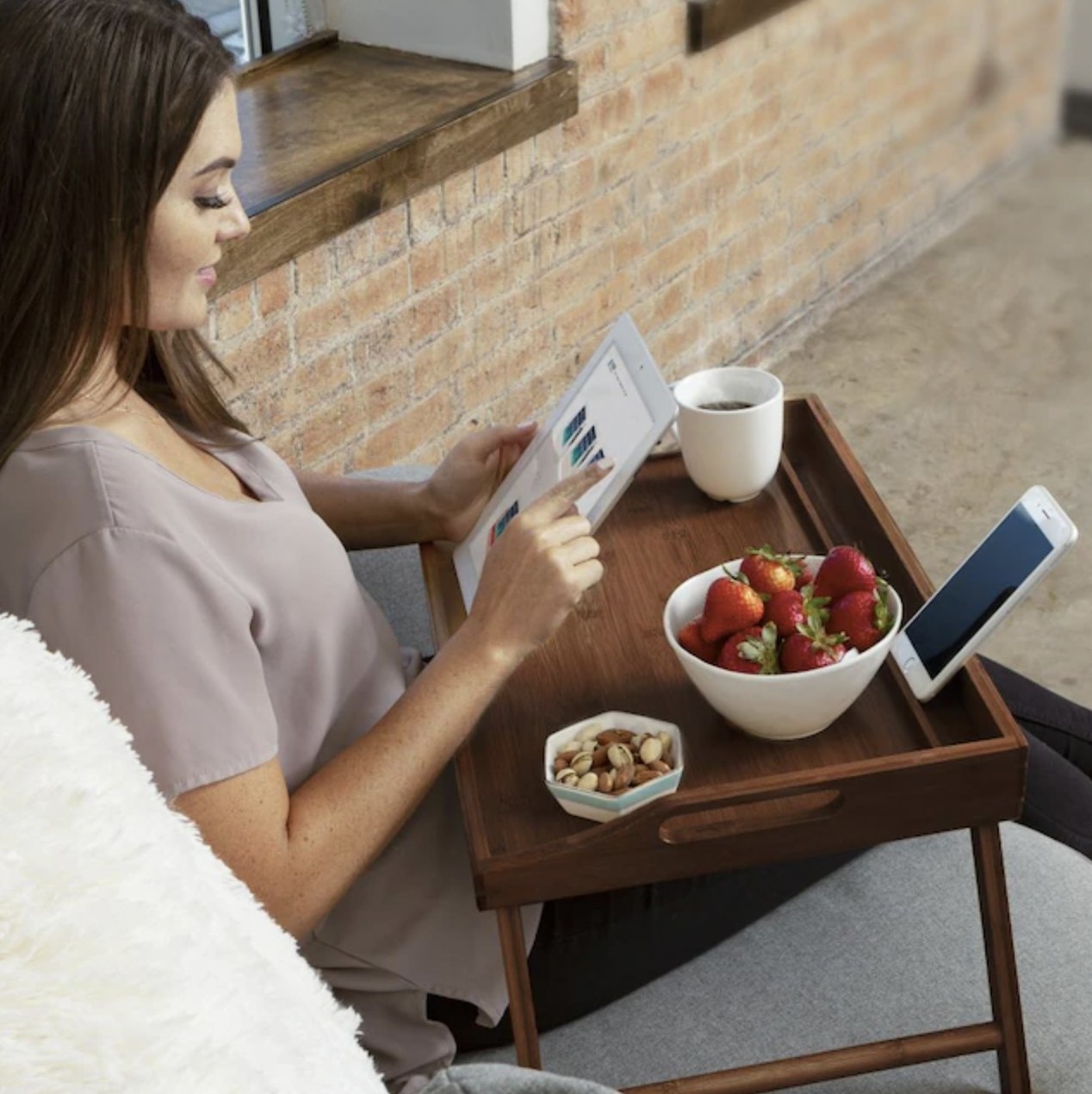 Model relaxing on bean bag with tray being used to hold tablet and phone, coffee and snacks