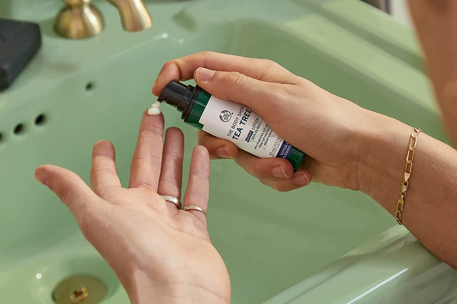 a person pumping some of the moisturizer onto their hand above a green sink
