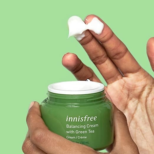 a hand with some of the product on it from the green tub of moisturizer