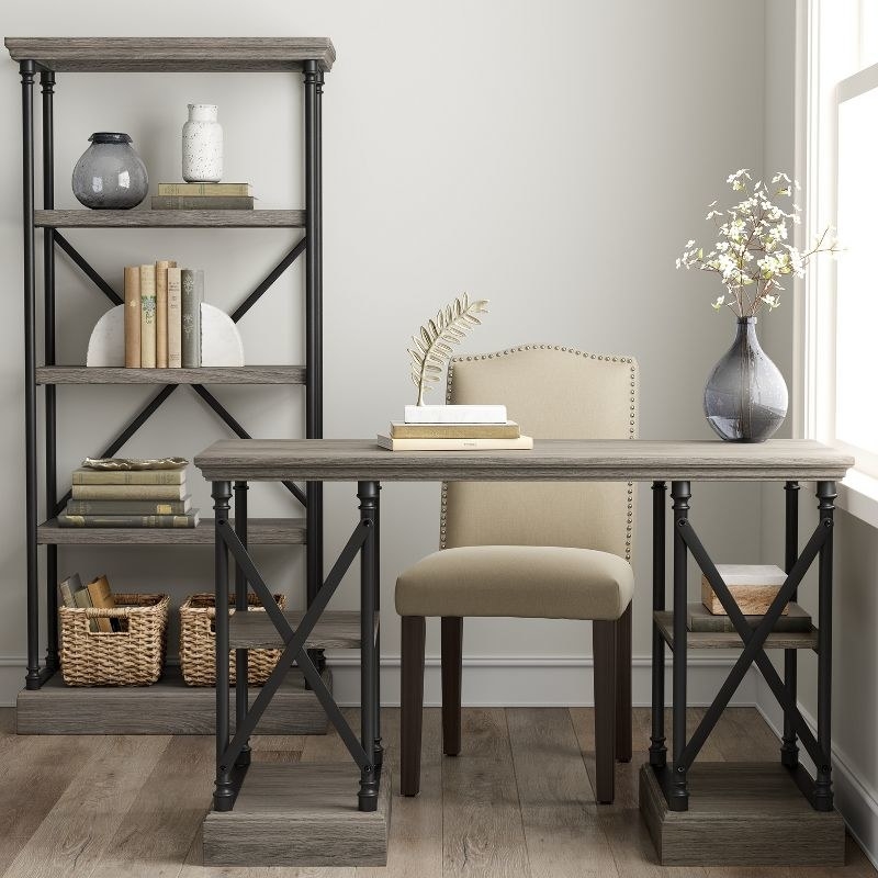 a wood writing desk in gray next to a tufted chair and bookcase