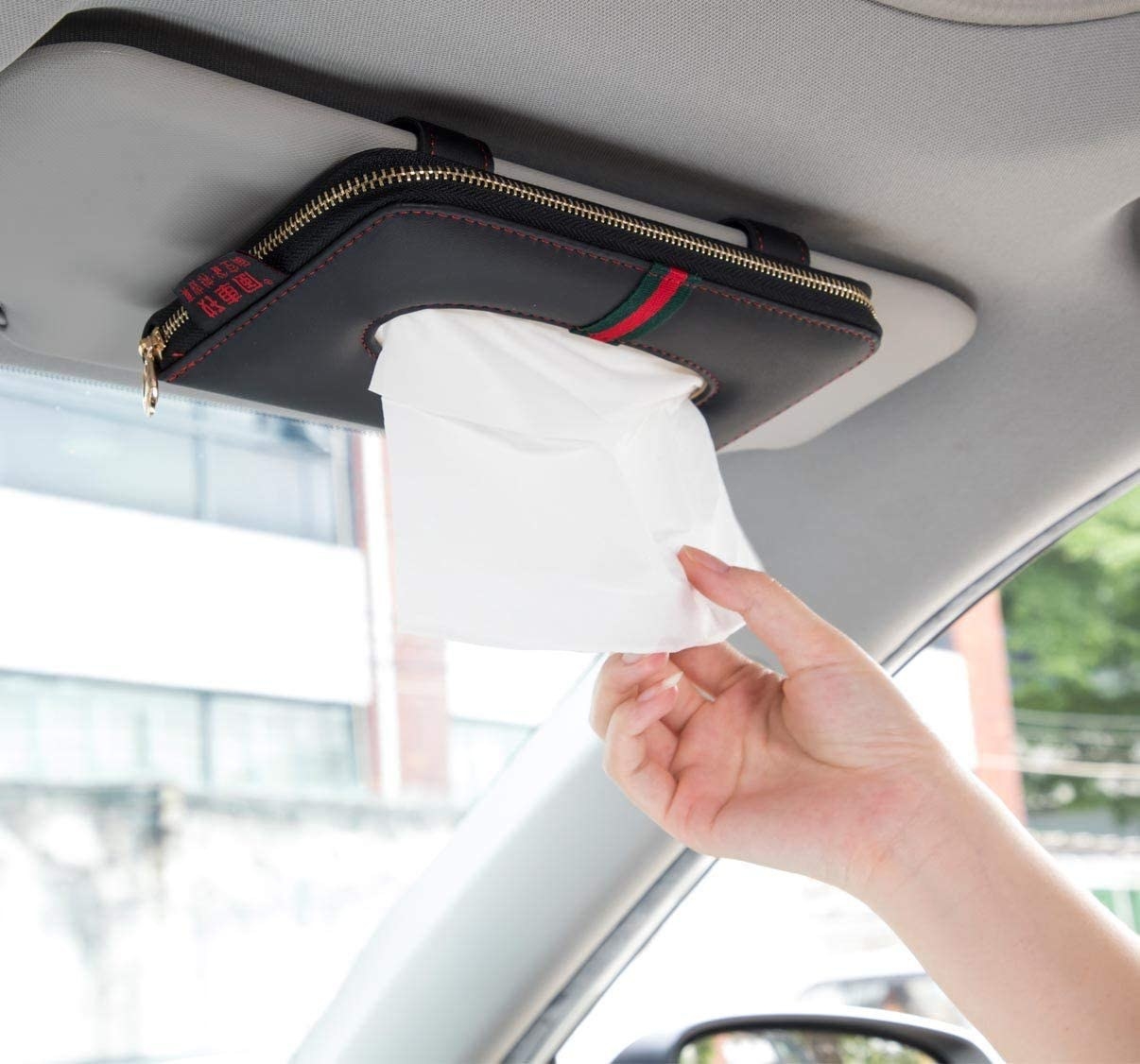 a person pulling a tissue out of the holder clipped to the visor in their car