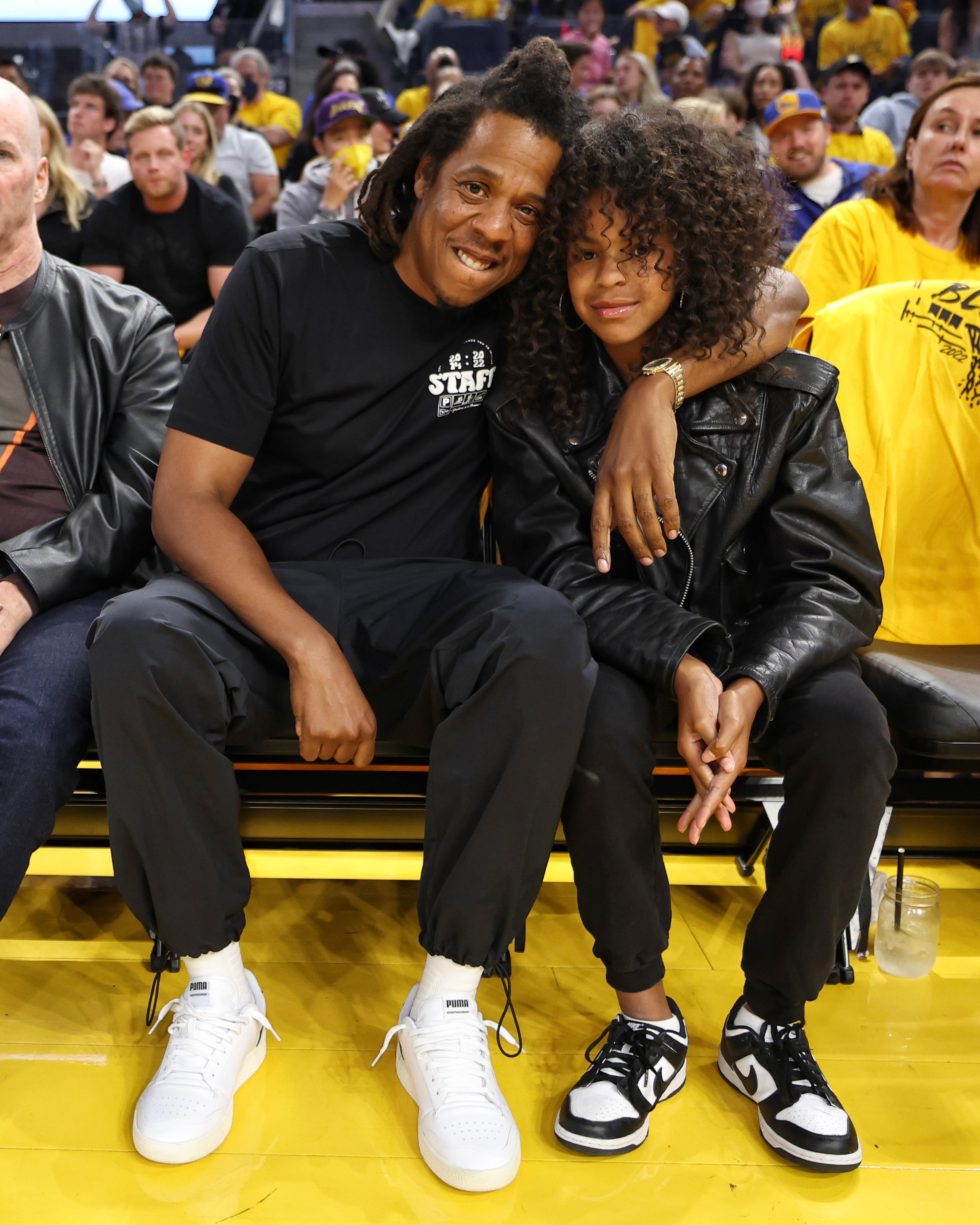 Jay-Z with his arm around Blue Ivy while sitting in courtside seats at a basketball game