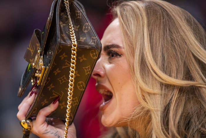 Adele yelling at a basketball game while covering her face with her purse