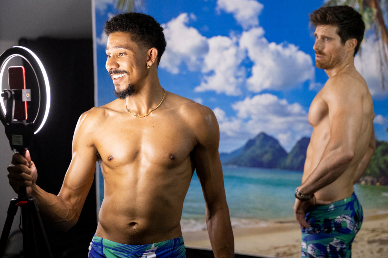 Keiynan Lonsdale and his character&#x27;s boyfriend pose shirtless in front of a ringlight and a tropical island backdrop