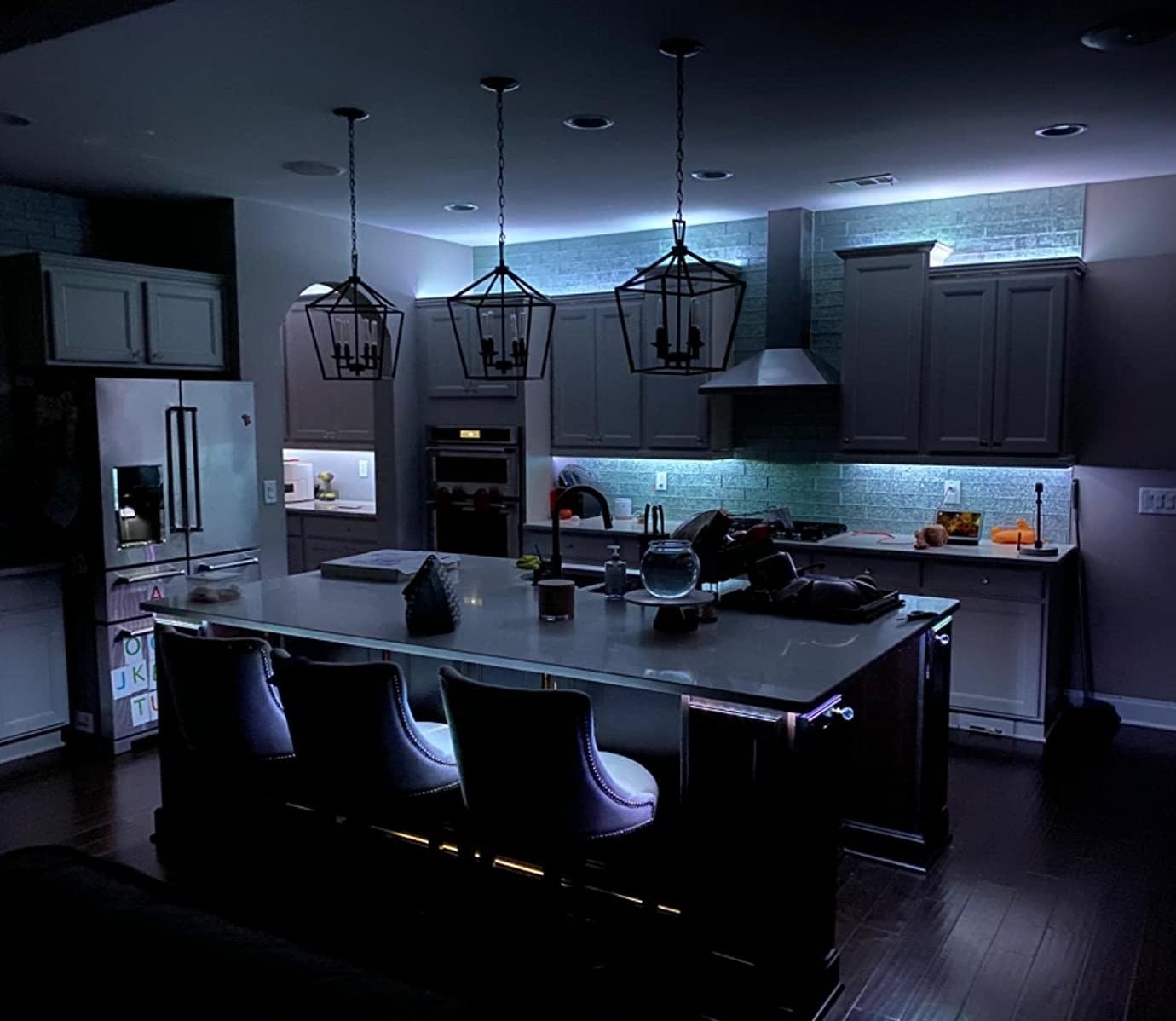 reviewer photo of the lights placed above and below their kitchen cabinets, illuminating them in light blue