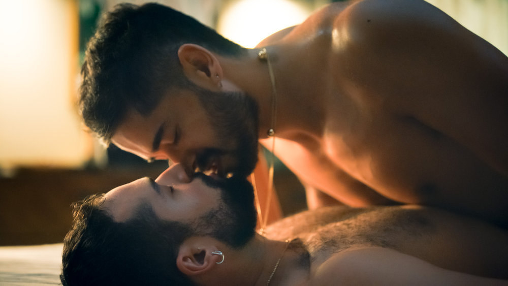 Johnny Sibilly and Chris Renfro kiss naked on a bed.