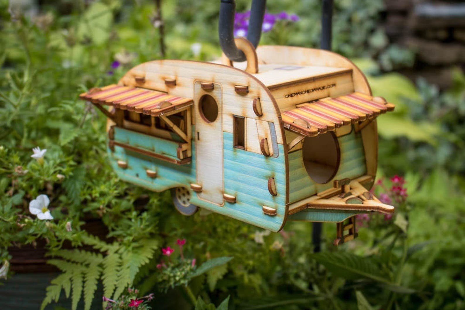 The vintage camper birdhouse in blue hanging with plants in the background