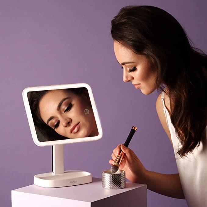 A person using the makeup mirror while applying powder