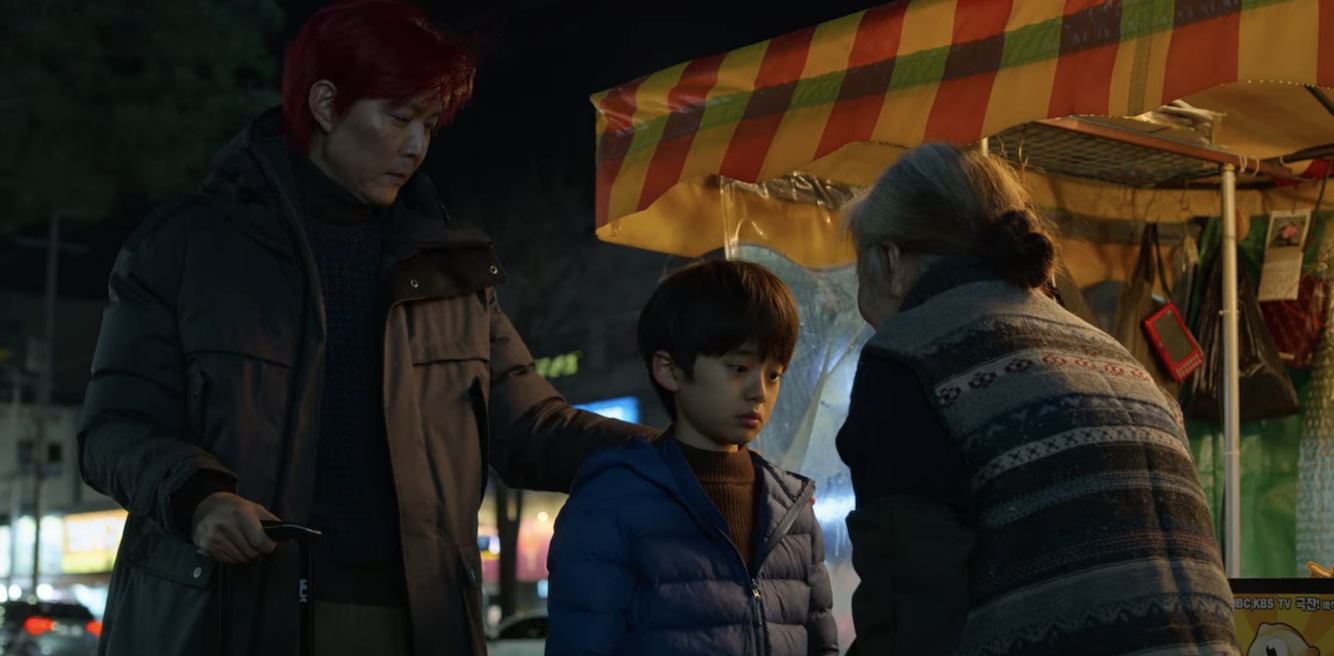 An elderly lady talking to a young boy, who&#x27;s with Gi-hun