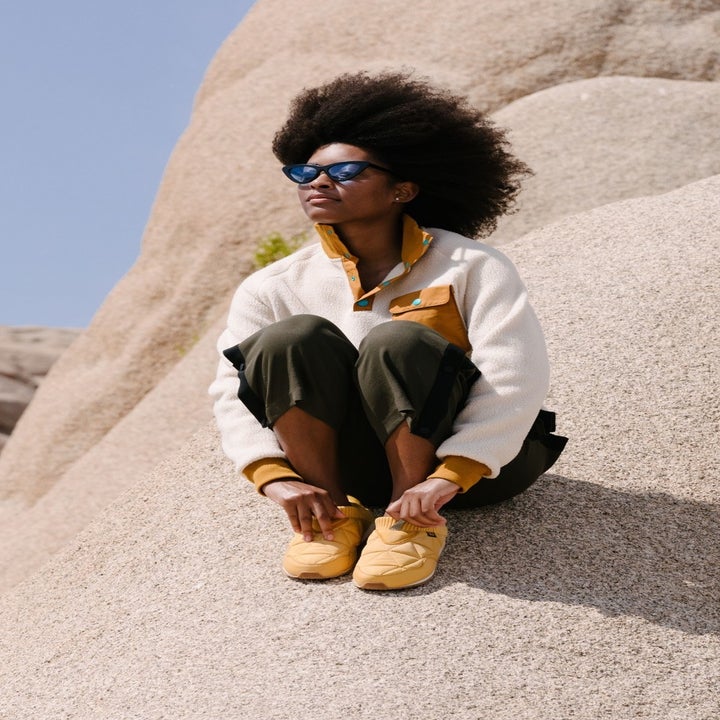 a model sitting on a rock in Joshua Tree wearing the yellow shoes