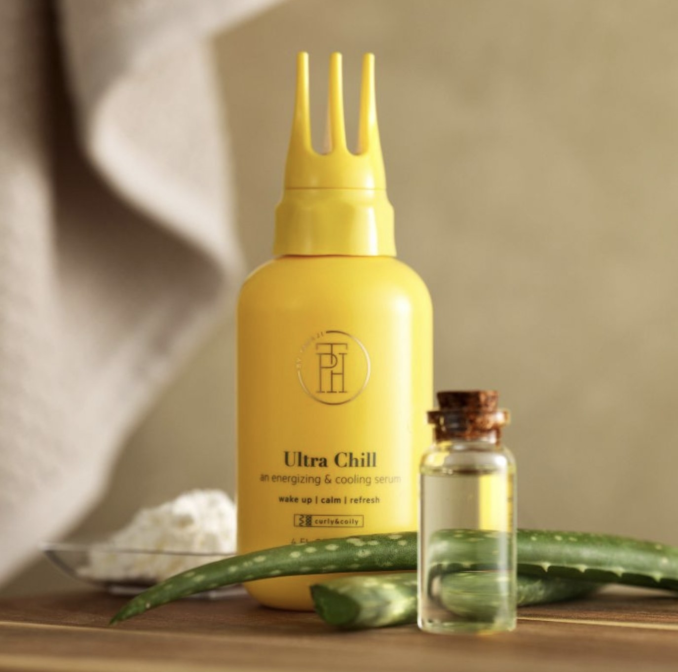 A bottle of hair serum with an aloe plant and a bottle with oil