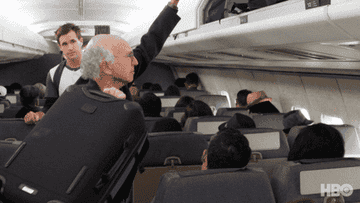 a character throwing a bag in the overhead bin on a flight