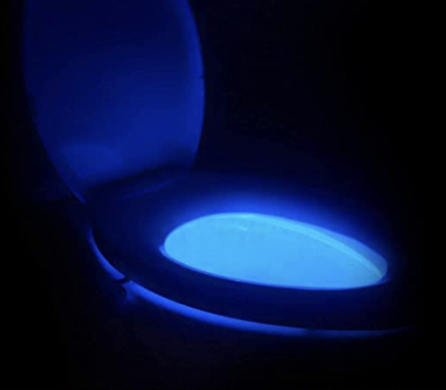 A toilet in the dark with the lamp illuminating the inside with a soft glow